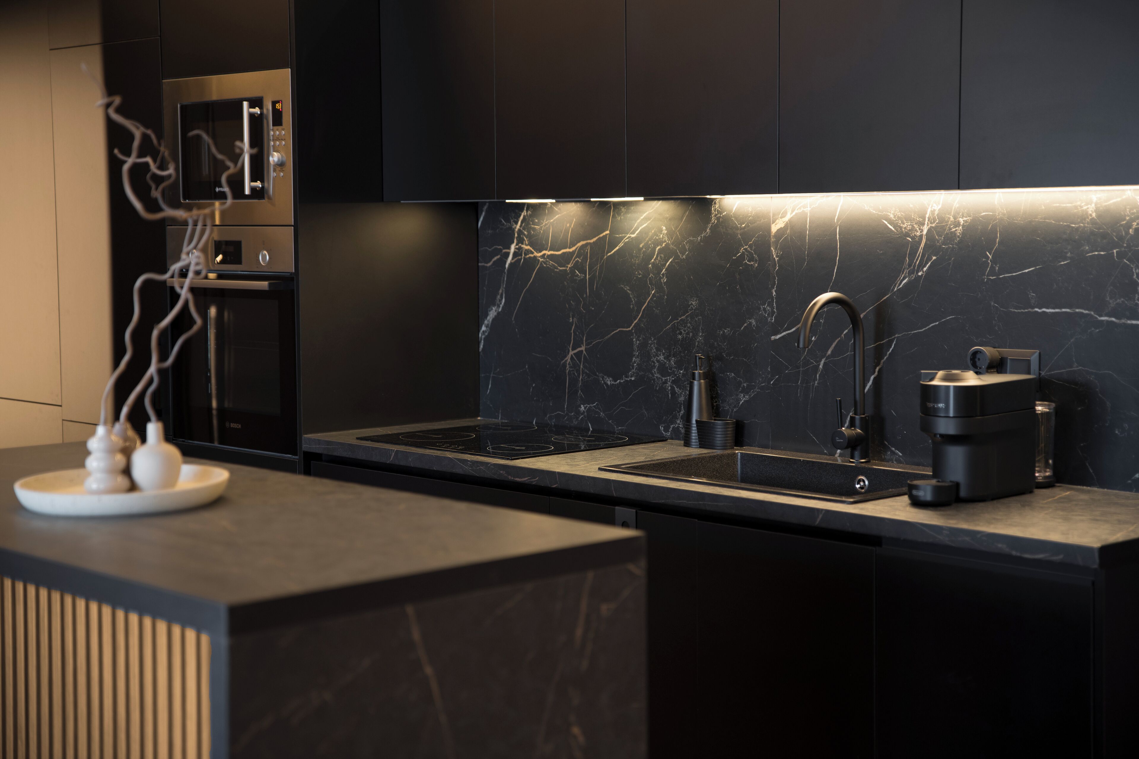 A modern kitchen with a sleek black countertop, a built-in microwave, and a marble backsplash.