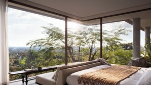 A bedroom with a large window, a bed, a bedside table, and a view of a forested landscape. - Amaya Kampot (Kampot)