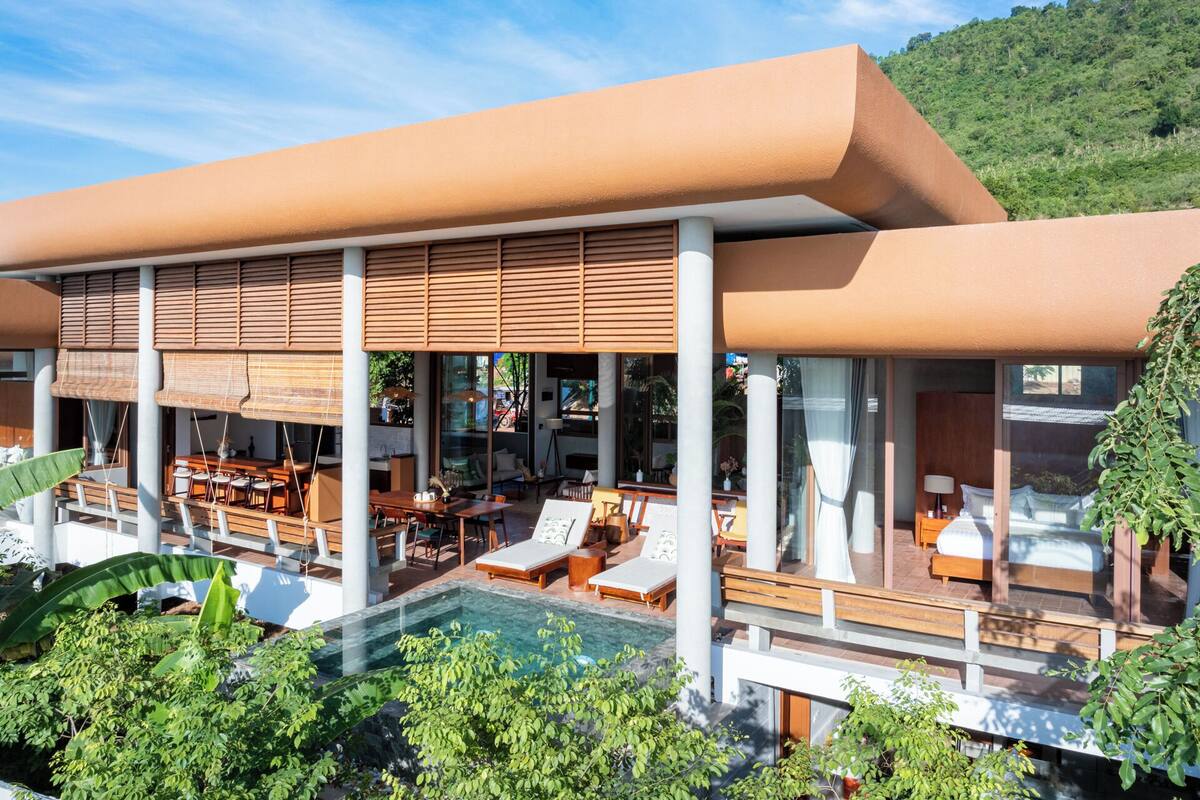 A modern resort with a pool, outdoor seating, and a view of the surrounding greenery.