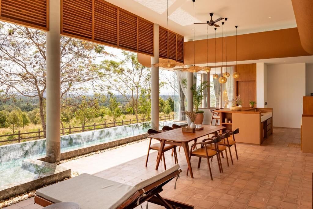 A spacious dining area with a view of a natural landscape, a pool, and a modern kitchen.