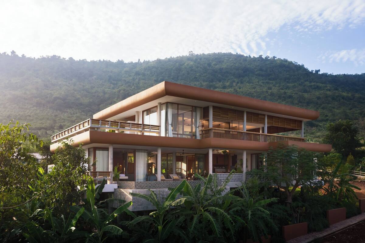 A modern two-story building with large windows, a balcony, and a lush garden in front.