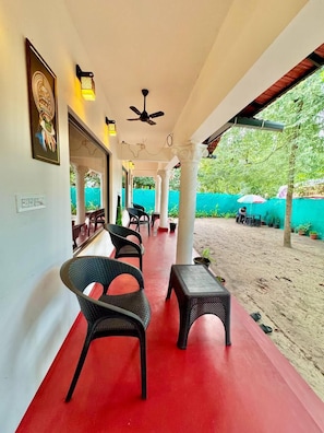 Un espace extérieur abrité, aménagé avec des chaises et des tables en osier, un ventilateur de plafond et offrant une vue sur la verdure environnante.