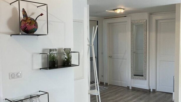 A modern interior with white walls, wooden flooring, and a minimalist design. There are shelves with decorative items and a ladder leaning against the wall. - Appartement 76m² 2 chambres, parking et jardin (Aix-les-Bains)