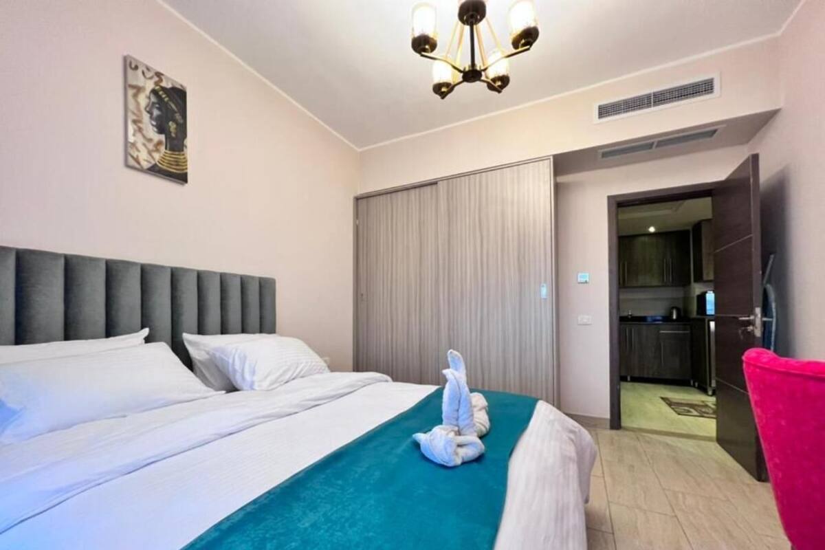 Une chambre d’hôtel avec un grand lit, une tête de lit, un lustre, une sculpture faite de serviettes, une porte donnant sur une salle de bain et un fauteuil rouge.