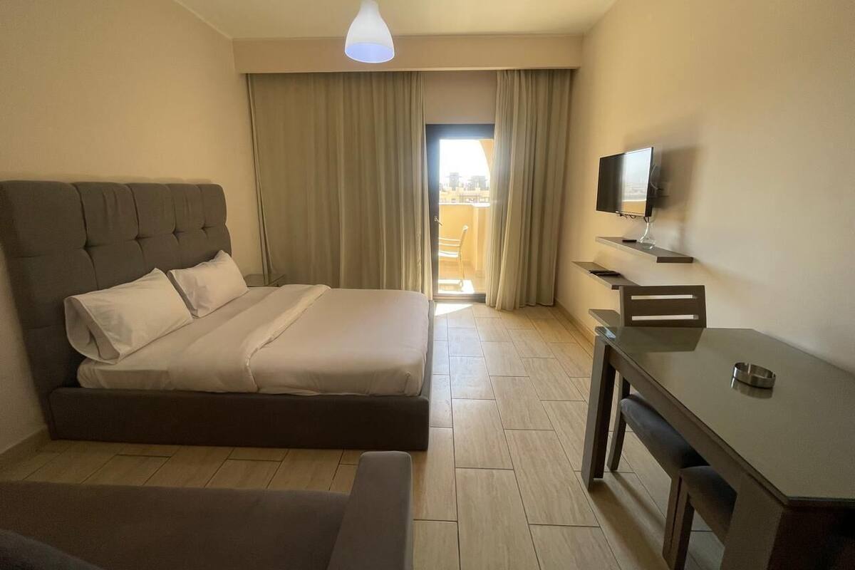 Une chambre à coucher avec un lit, un bureau, une chaise, un téléviseur et une fenêtre avec des rideaux.