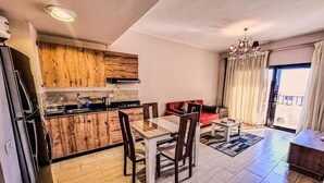 A modern kitchen with wooden cabinets, a dining area with a table and chairs, a red sofa, and a chandelier. - Al Dau Heights Apartments (Hurghada)