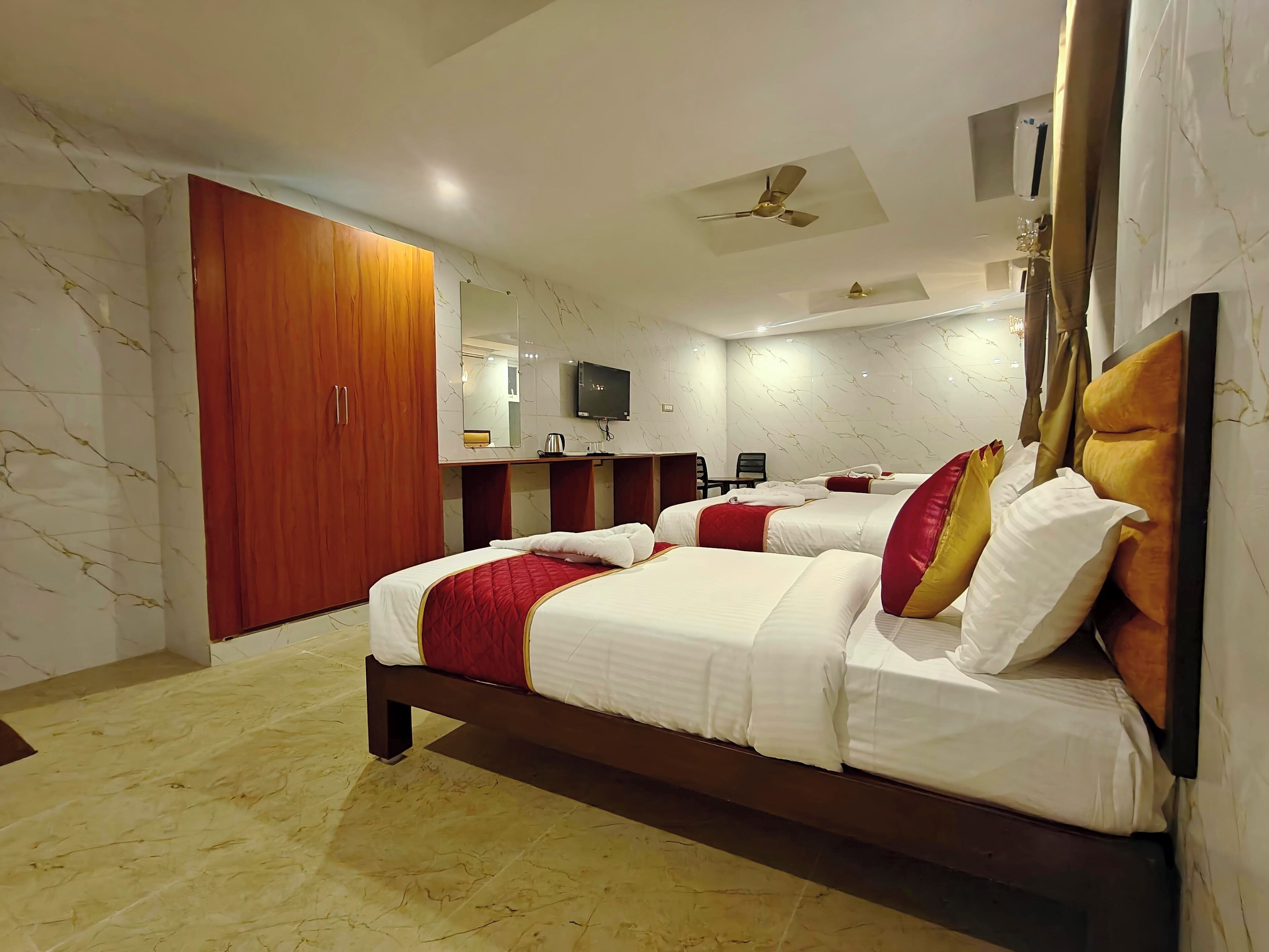 Habitación de hotel con una cama grande, un armario de madera, un escritorio con silla, un televisor y un ventilador de techo.