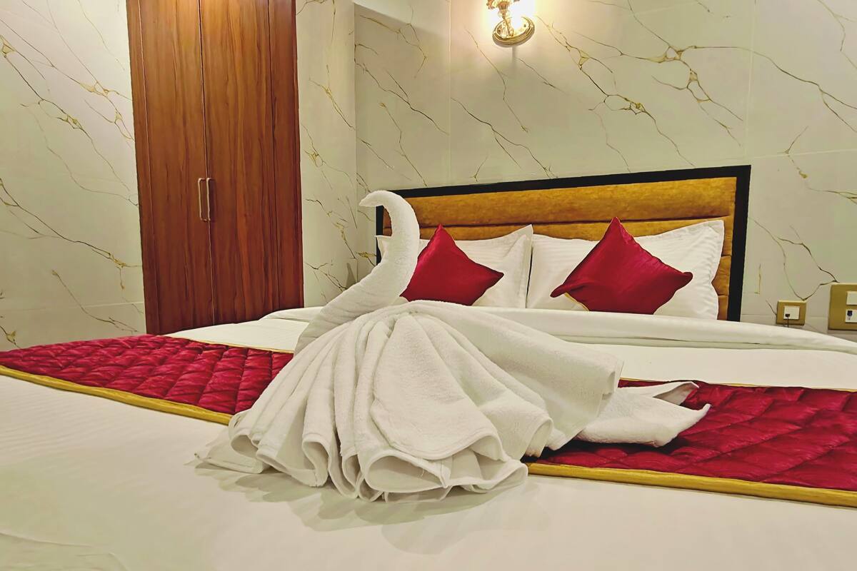 Una cama bien hecha con una colcha roja y blanca, un cabecero de madera y una pared con estampado de mármol.