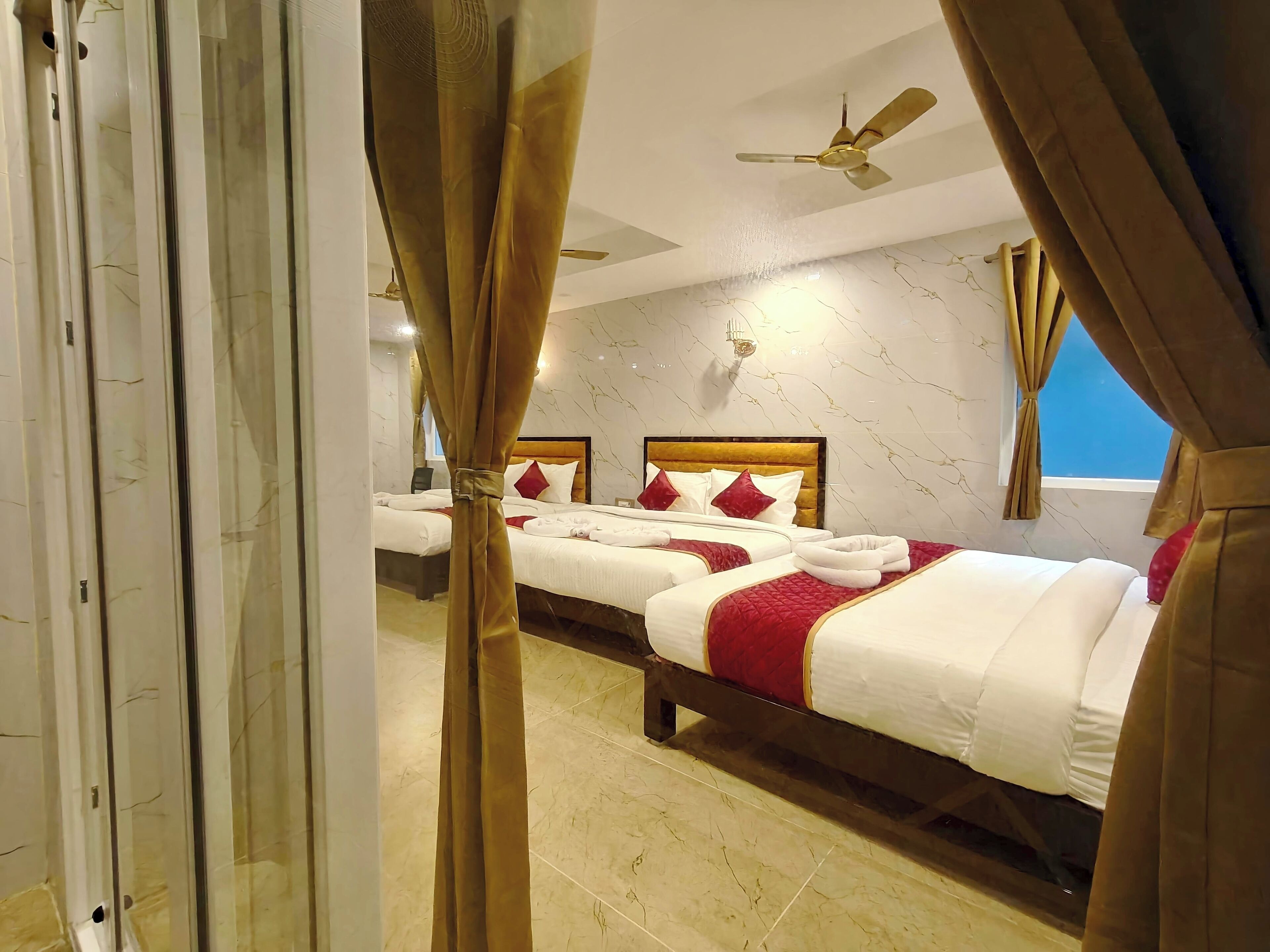 A hotel room with two beds, a ceiling fan, marble walls, and a view of the sky.