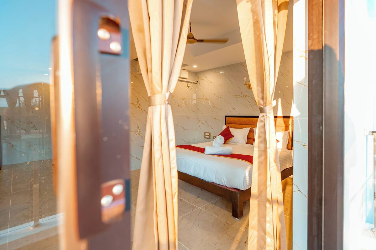 Habitación de hotel con cama, cortinas, ventilador de techo y vistas por una puerta de cristal.
