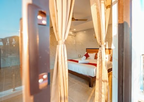 Ein Hotelzimmer mit einem Bett, Vorhängen, einem Deckenventilator und Blick durch eine Glastür.