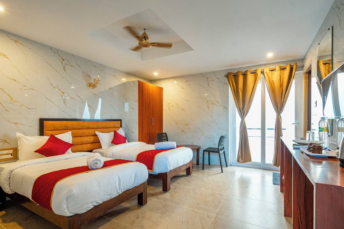 Habitación de hotel con dos camas, ventilador de techo, armario de madera, una mesita y vistas al exterior.