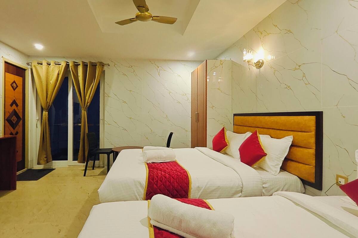 Habitación de hotel con dos camas, un ventilador de techo, una pared de mármol y una ventana con cortinas.