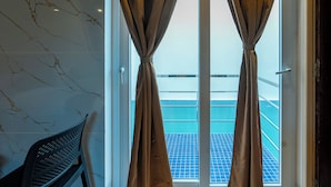 Quarto com vista para uma varanda com azulejos azuis, uma cadeira e cortinas.