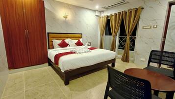 A bedroom with a bed, a wardrobe, a ceiling fan, an air conditioning unit, a dining table with chairs, and a view through the window.