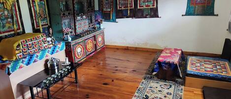 Una habitación tradicional con suelo de madera, una rueca de oración y coloridas banderas de oración.