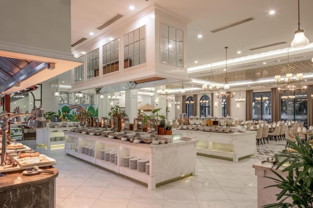 Un'ampia hall dell'hotel con soffitto alto, un'area buffet centrale e un salotto con tavoli e sedie.