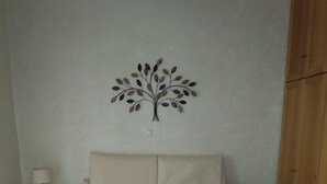 Ein Doppelbett mit schlichtem Bettbezug, eine Wanddekoration mit Baummotiv, ein Nachttisch mit Lampe und ein Korb voller Muscheln auf dem Boden.