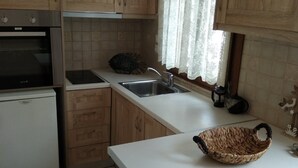 Eine Küche mit Holzausstattung, einer weißen Arbeitsplatte, einem Spülbecken, einem Herd und einem Fenster mit Spitzenvorhängen.