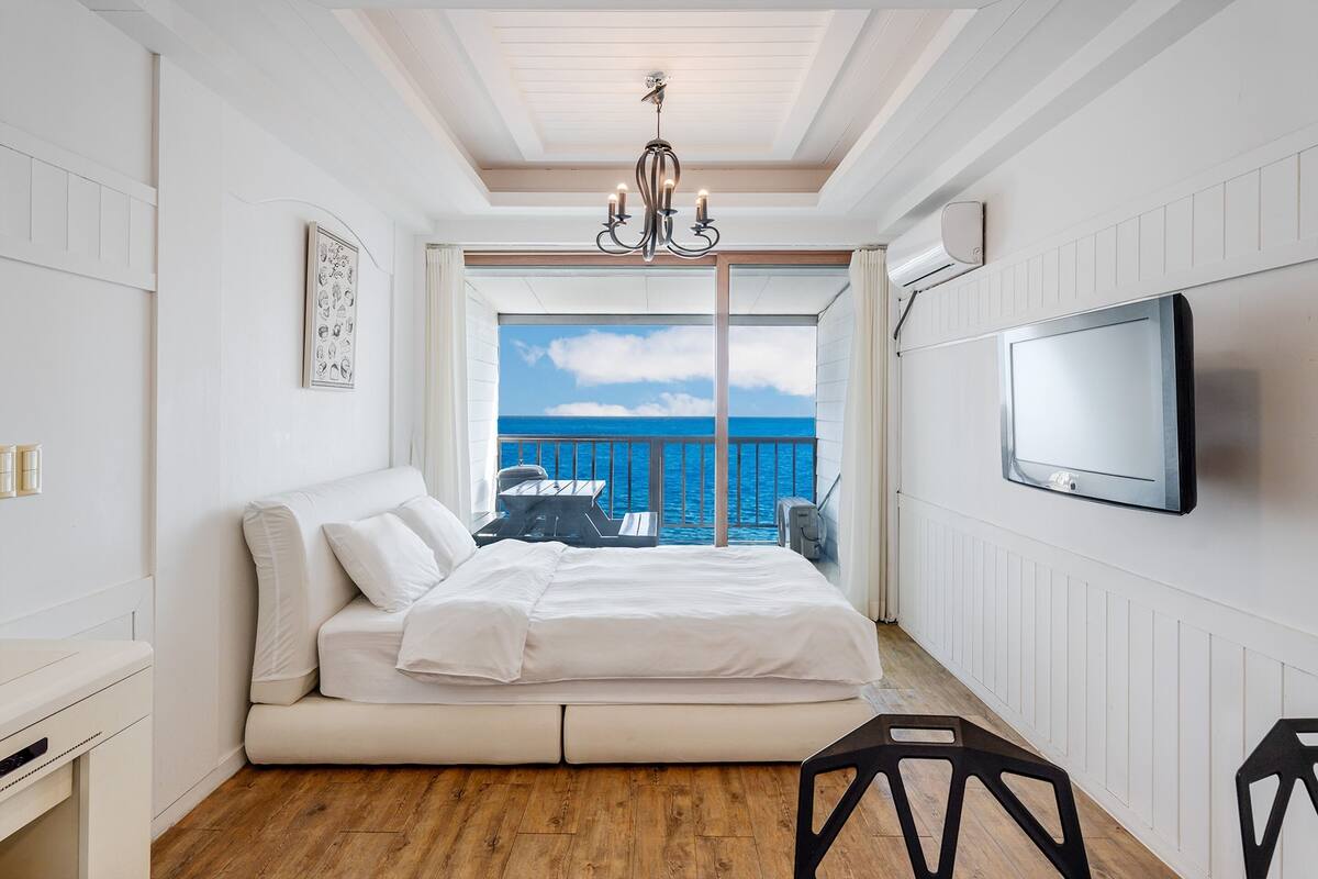 Une chambre à coucher avec un lit, une télévision, une vue sur la mer et un lustre.