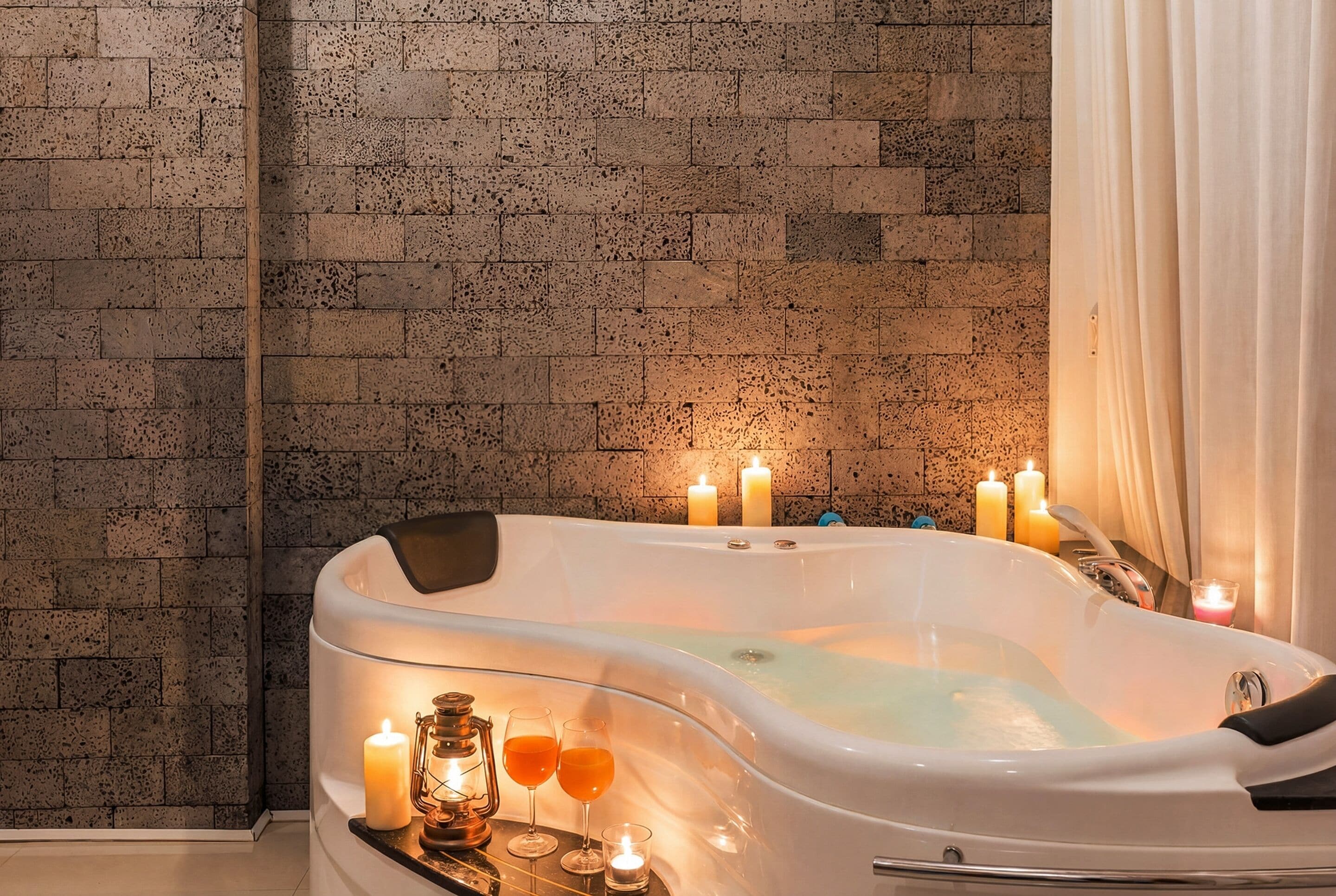 A spa room with a white bathtub, candles, and a tray with glasses and a candle.