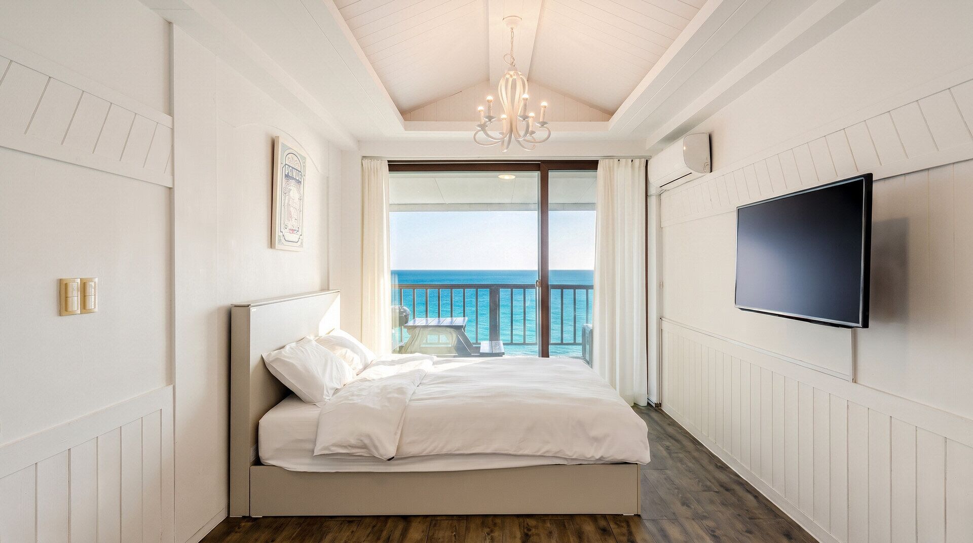 Quarto com cama, TV, lustre e vista para o oceano.