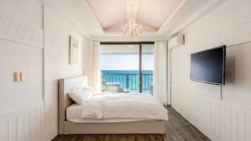 Quarto com cama, TV, lustre e vista para o oceano.