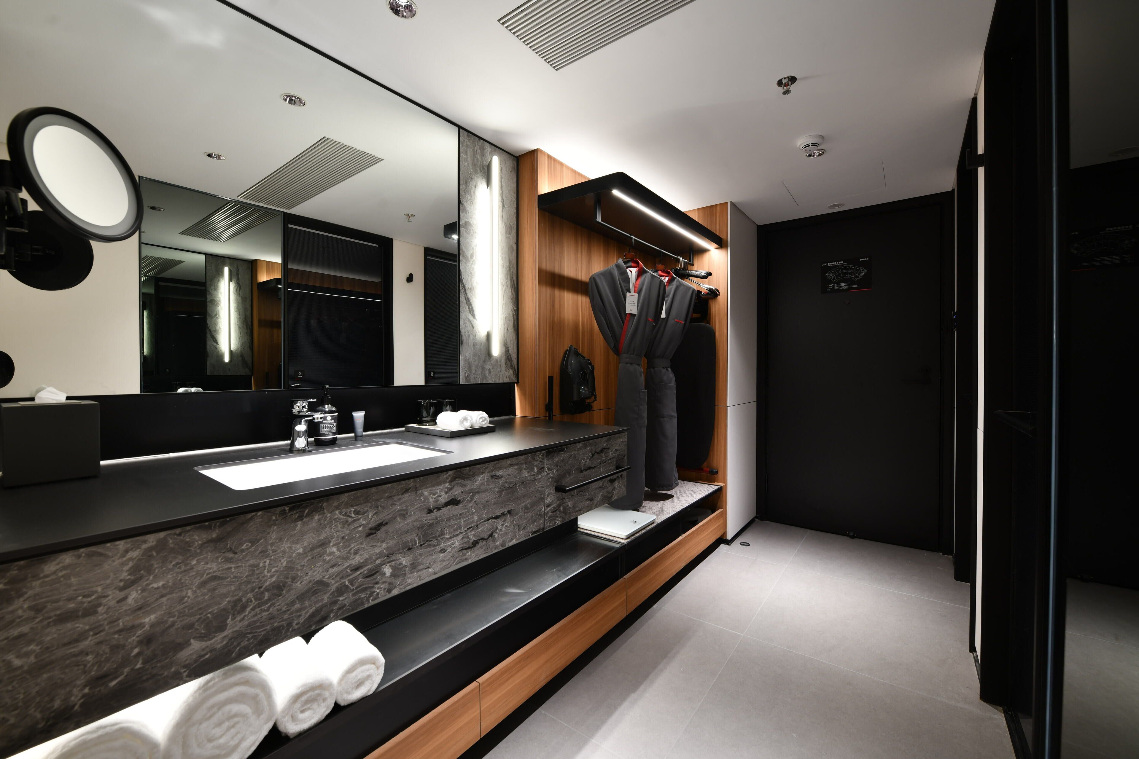 A modern bathroom with a large mirror, a sink, and a vanity. There are towels neatly rolled up on the counter.