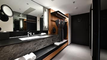 A modern bathroom with a large mirror, a sink, and a vanity. There are towels neatly rolled up on the counter.