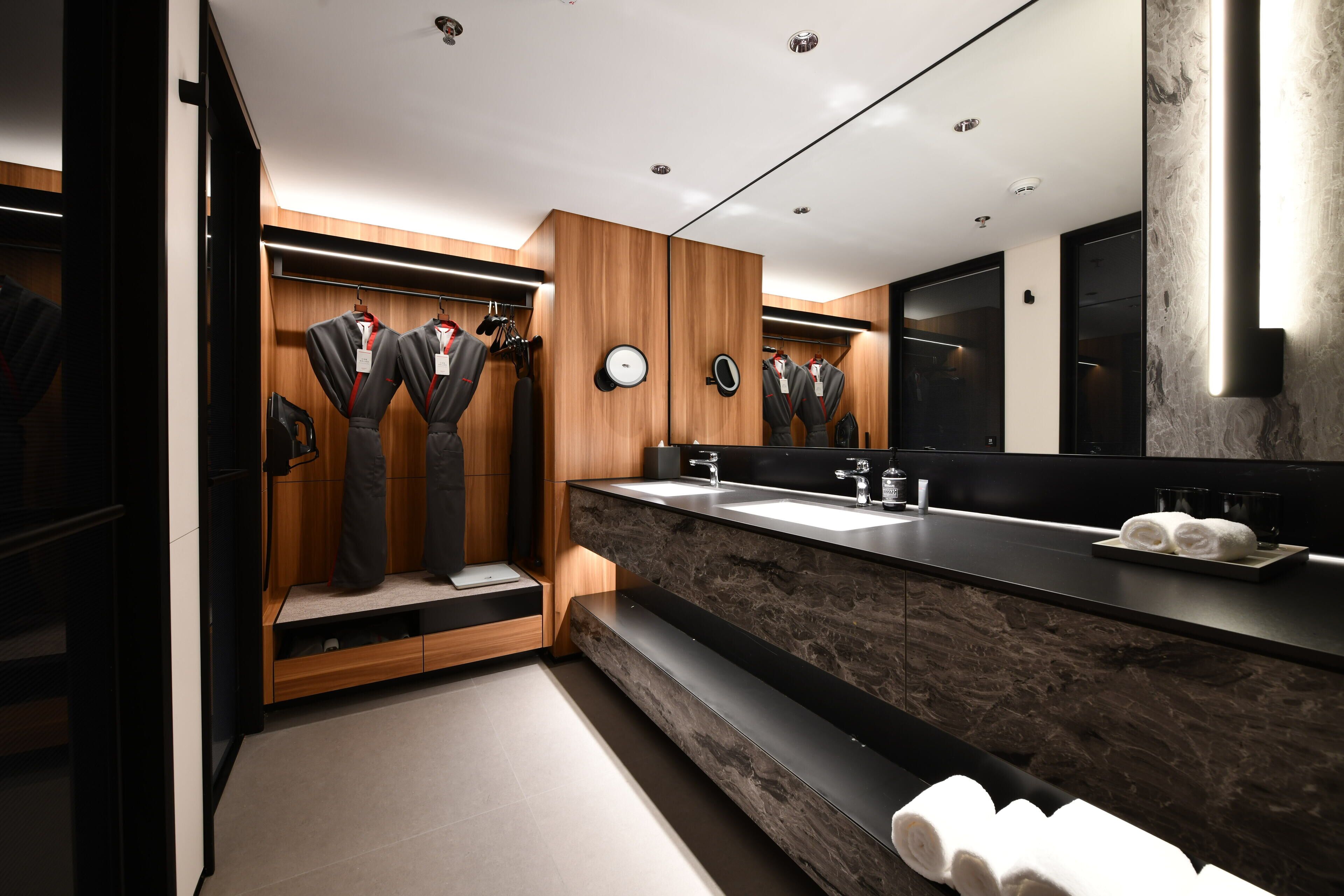 A modern bathroom with a large mirror, dark marble countertop, and wooden paneling.