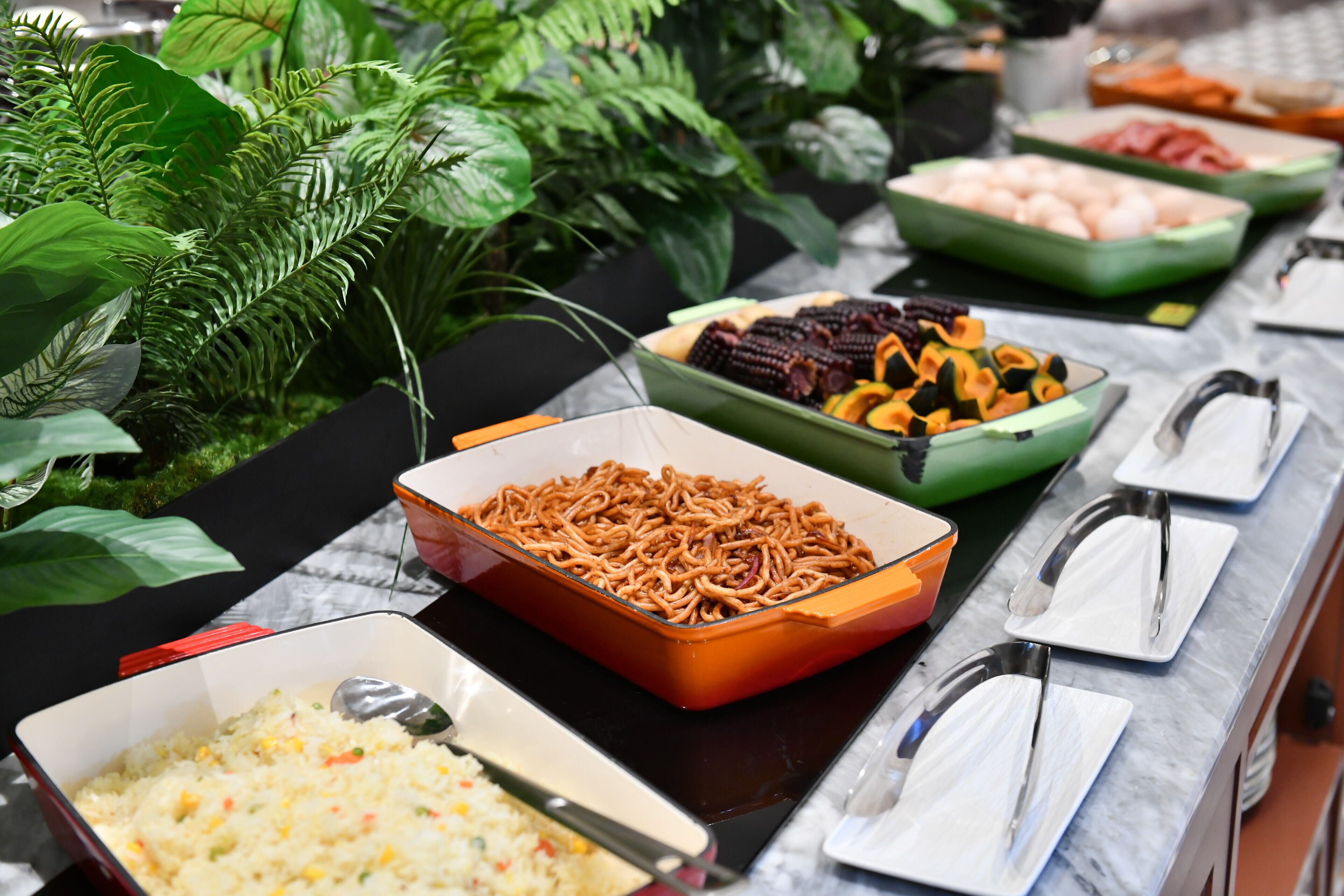 Un bufé con diversos platos, incluyendo arroz, fideos y verduras, dispuestos sobre una mesa con encimera de mármol.