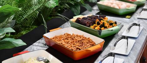 Un bufé con diversos platos, incluyendo arroz, fideos y verduras, dispuestos sobre una mesa con encimera de mármol.