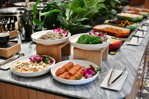 A buffet with various dishes, including a plate of sliced meat, a bowl of green salad, and a dish with pink flowers.