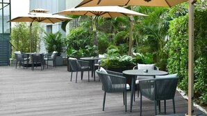 An outdoor patio area with round tables and chairs, surrounded by lush greenery and large umbrellas. - IntercityHotel Shenzhen Huaqiang North (Shenzhen)