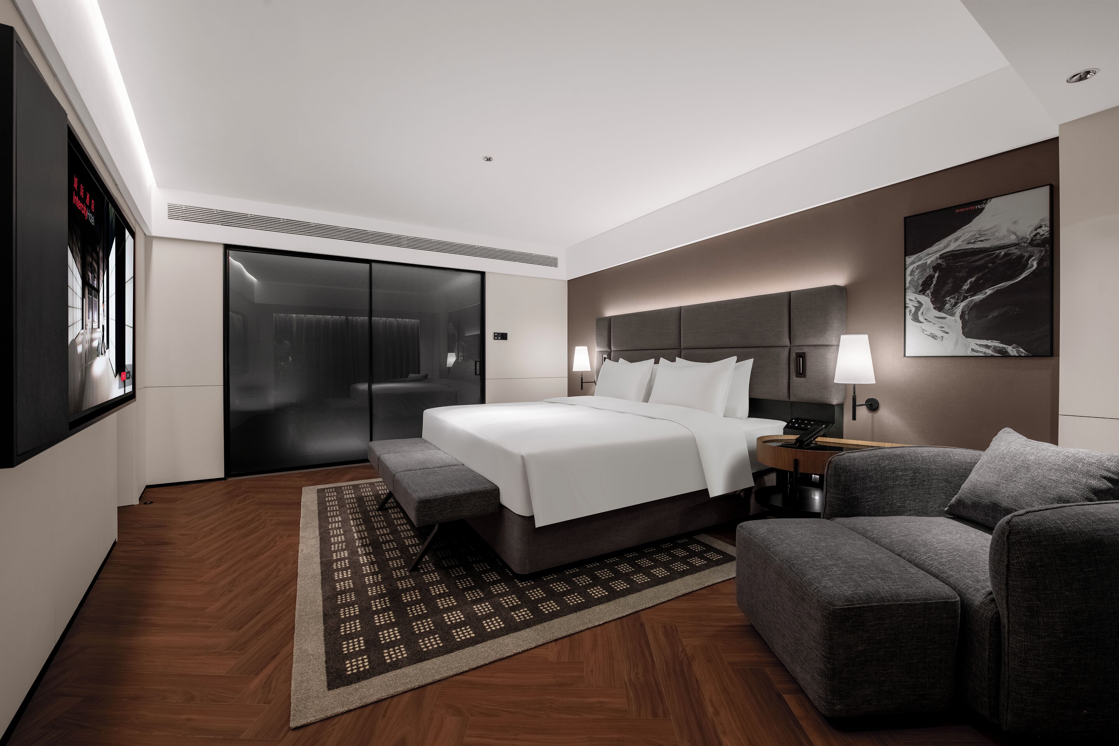 Ein modernes Hotelzimmer mit einem großen Bett, einer Couch, einem Schreibtisch mit Lampe, einem Fernseher und einem Schiebetürenschrank.