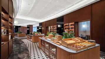 Un moderno vestíbulo de hotel con piso de mármol, paneles de madera y una zona de bufé con diversas opciones de comida.