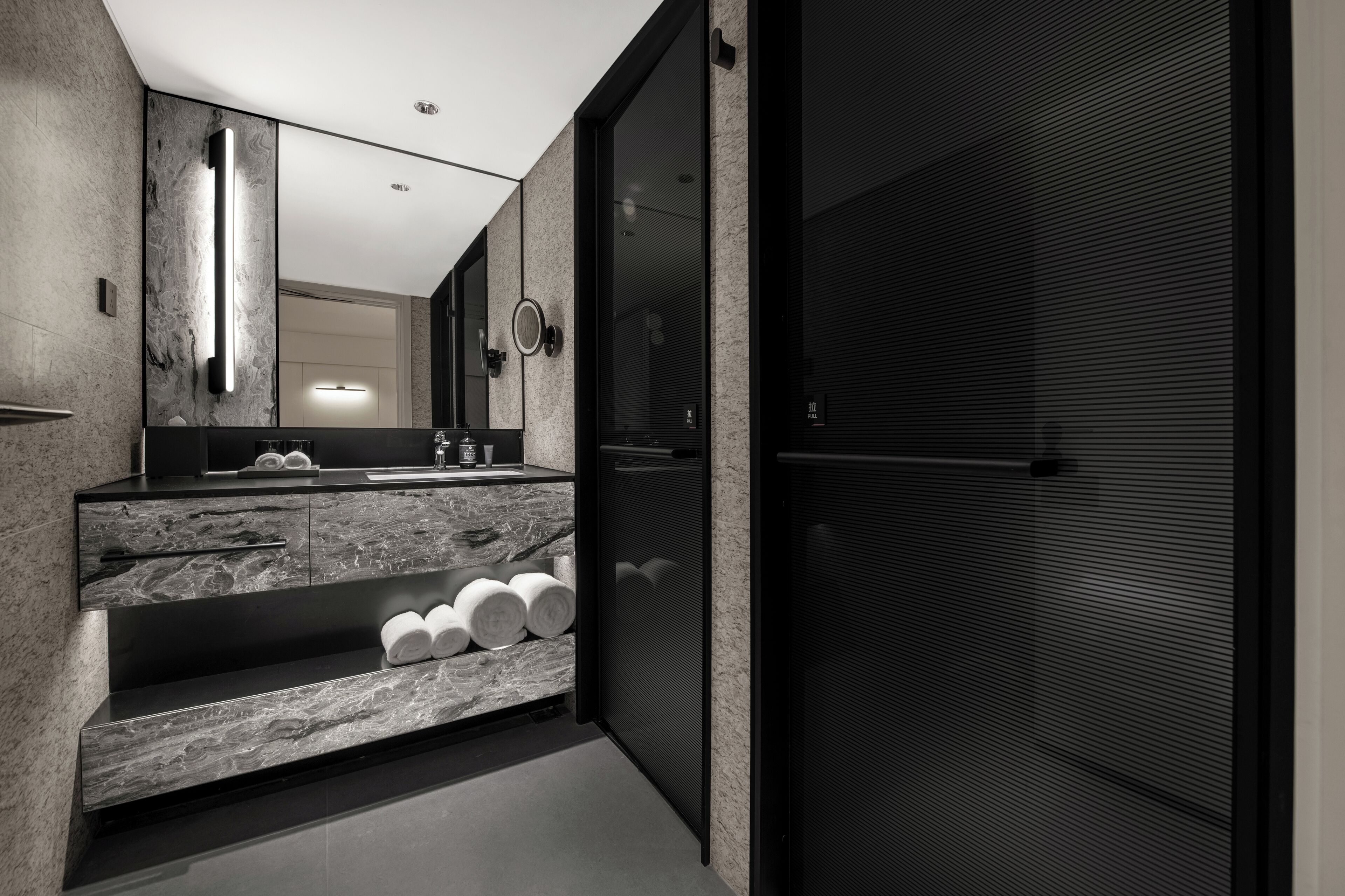 A modern bathroom with a marble vanity, a large mirror, and a towel rack.