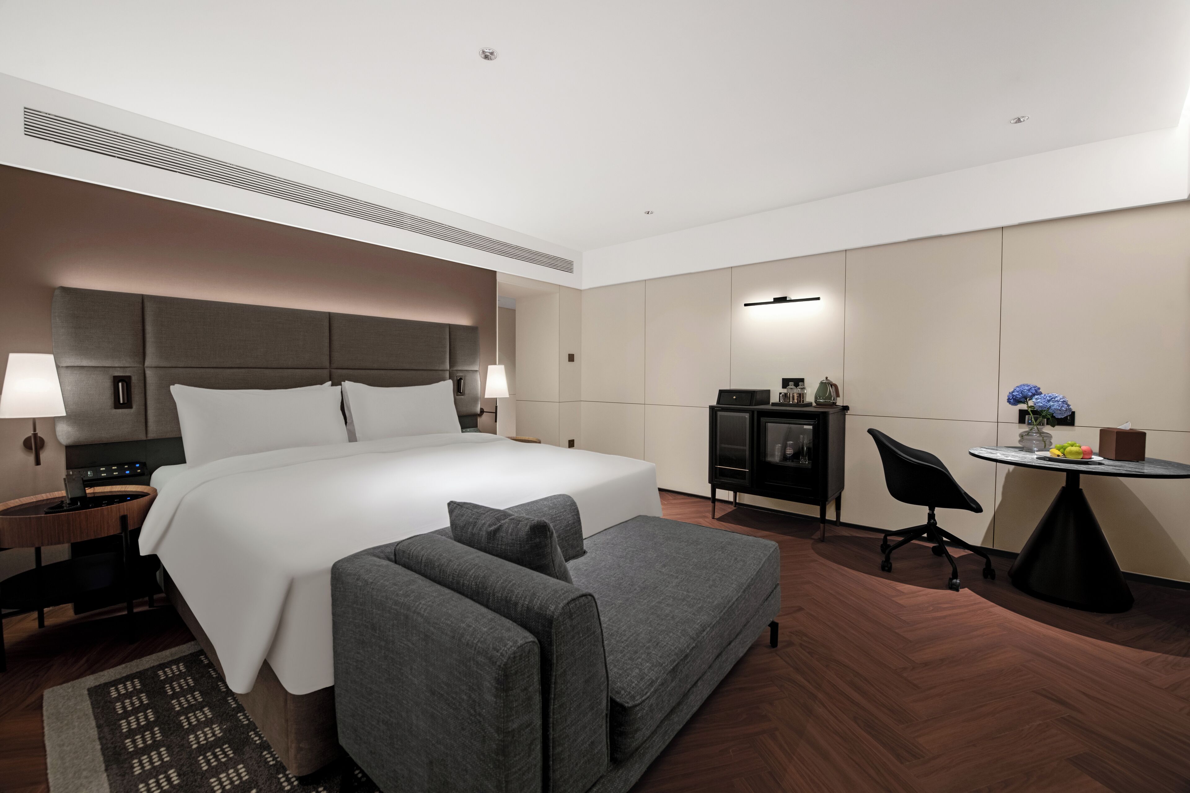 A modern hotel room with a large bed, a sofa, a desk, and a chair.