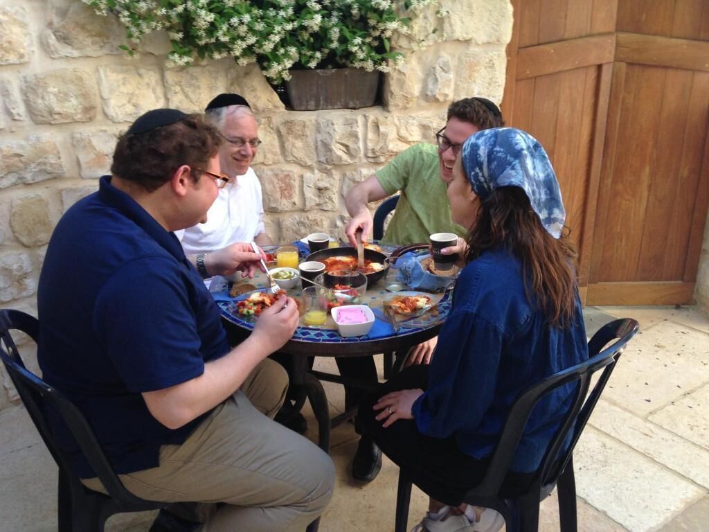 Un grupo de personas cenando al aire libre en una mesa redonda, con diversos platos y bebidas.