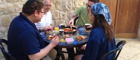 Un grupo de personas cenando al aire libre en una mesa redonda, con diversos platos y bebidas.