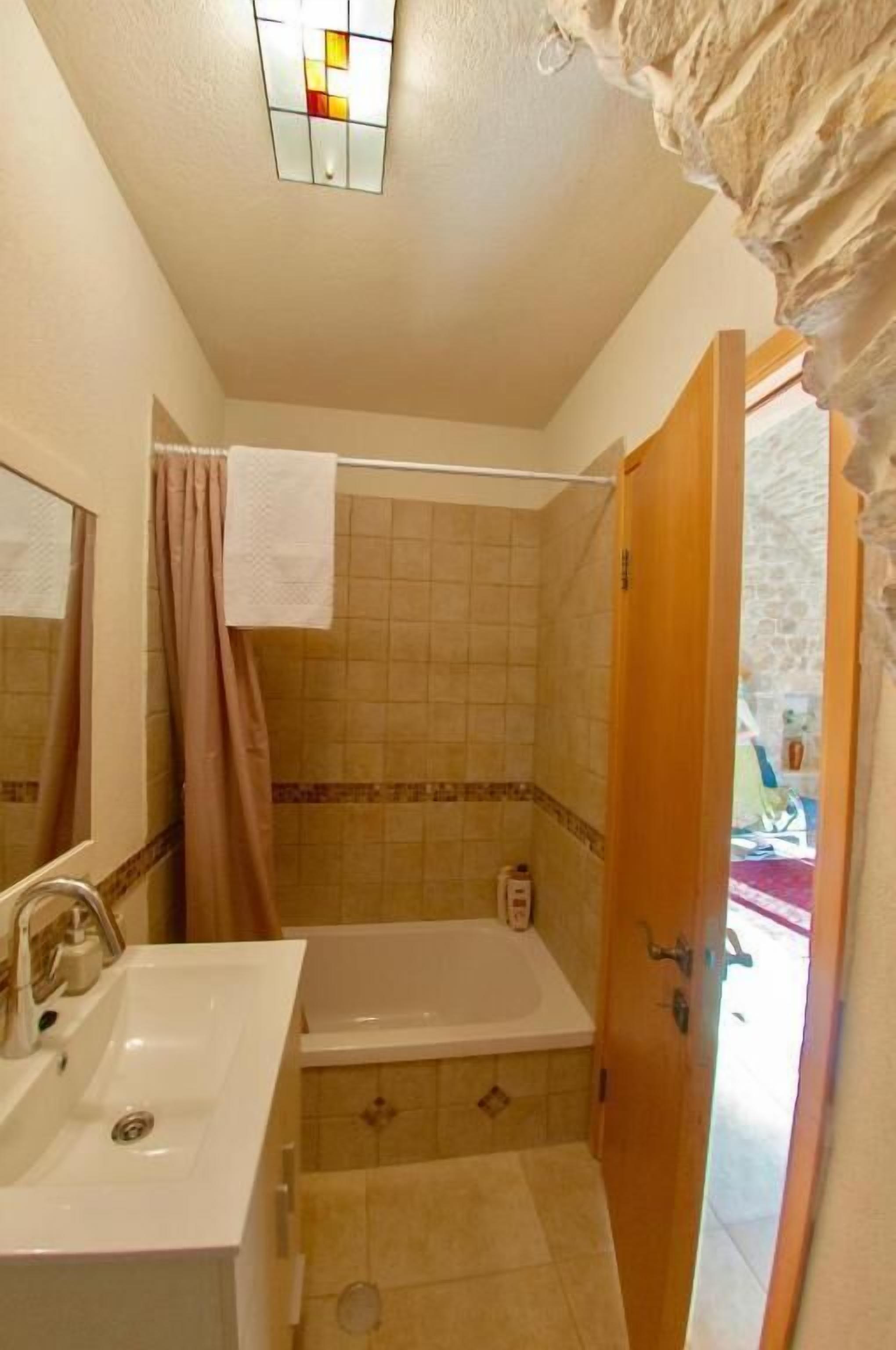 A bathroom with a sink, mirror, shower, and a door leading to another room.