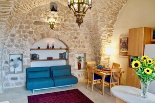 Uma sala de estar acolhedora com parede de pedra, um sofá azul, uma mesa de jantar com cadeiras e um vaso de girassóis.