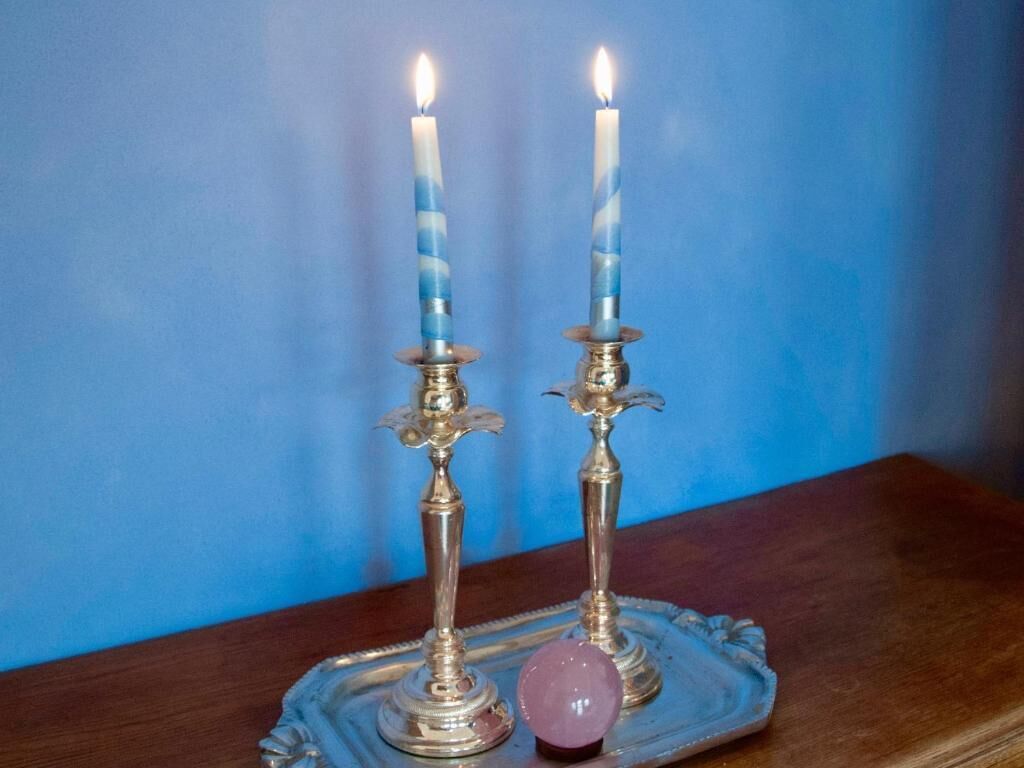 Deux bougies allumées sur un plateau en argent, accompagnées d’un objet décoratif.