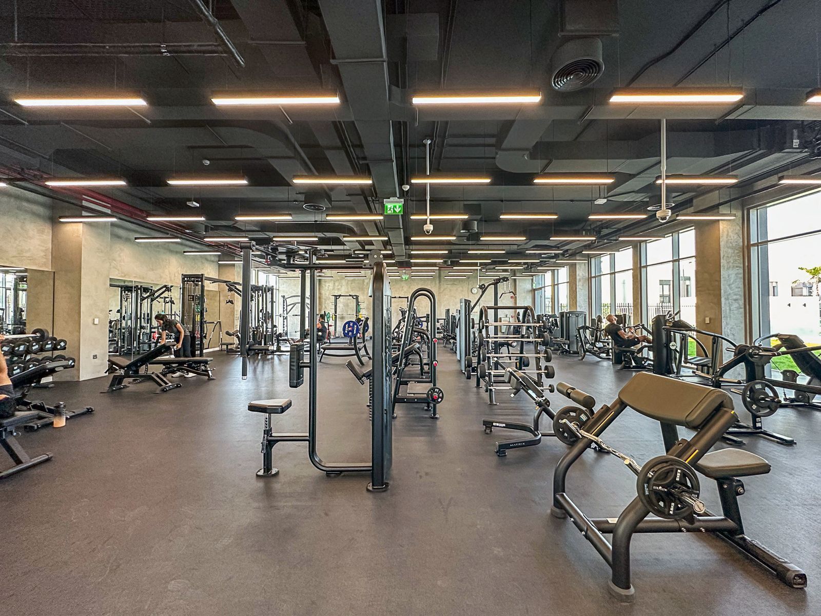 Een ruime fitnessruimte met diverse fitnessapparaten, grote ramen en een modern plafondontwerp.