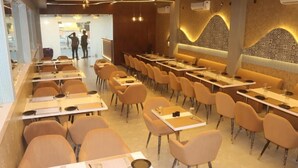 A restaurant with multiple tables and chairs, a patterned wall, and a modern ceiling design. - Hotel Cosmos (Bhubaneshwar)