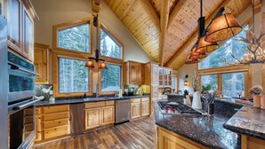 A spacious kitchen with wooden cabinets, a stainless steel oven, and a large island with a granite countertop. - Truckee Mountain Cabin with Hot Tub + Game Room + Forest Views | Gray Wolf Lodge (Truckee)