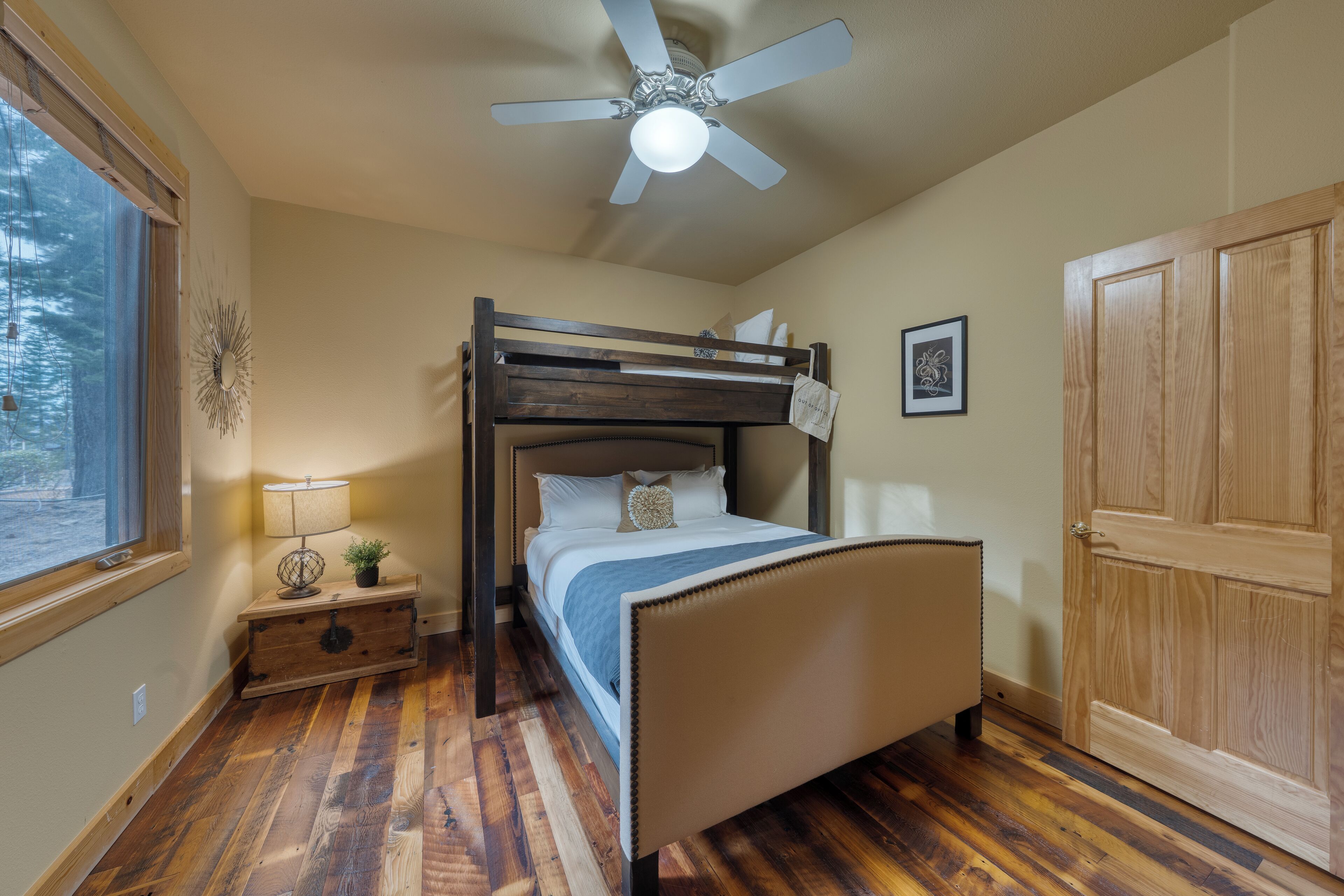 Un dormitorio con literas, una mesita de noche con lámpara, un ventilador de techo y una puerta de madera.
