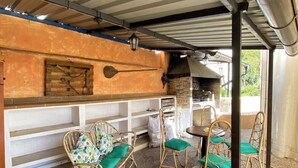 Een terras buiten met rieten stoelen, een stenen muur en een barbecuehoek.