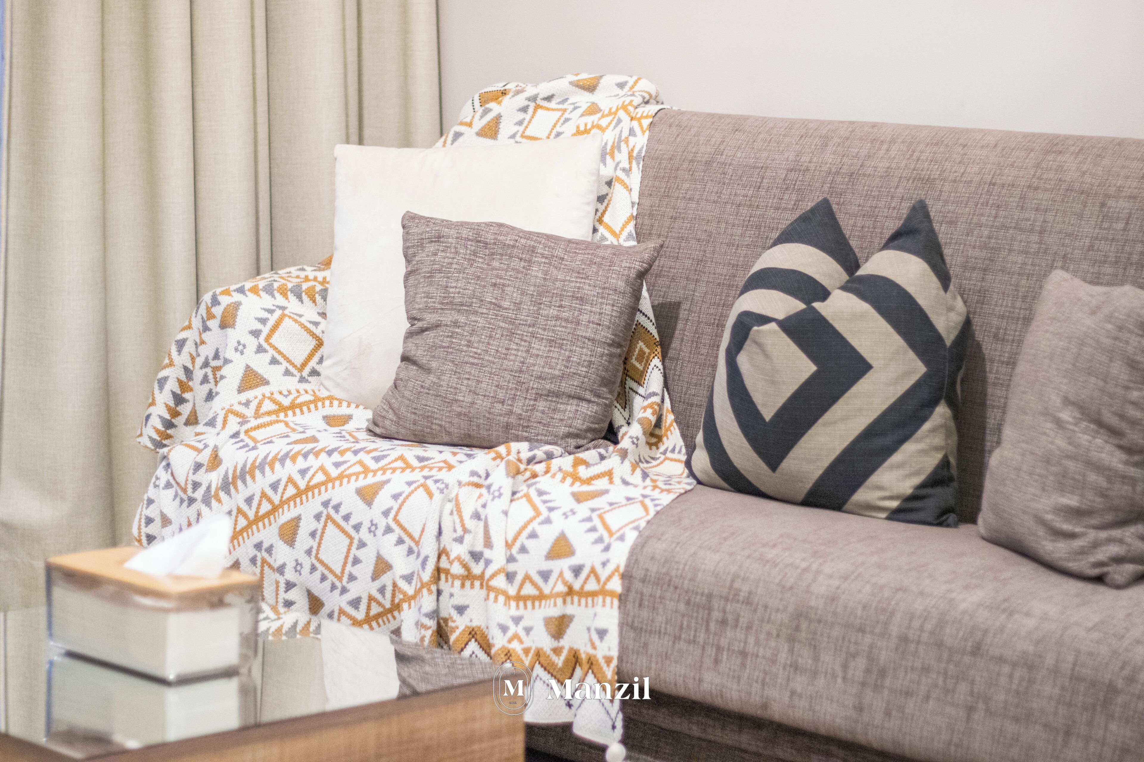 A living room with a sofa, patterned throw, and a tissue box.