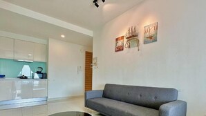 Ein modernes Wohnzimmer mit einem grauen Sofa, einem Glastisch und einer Küche im Hintergrund.